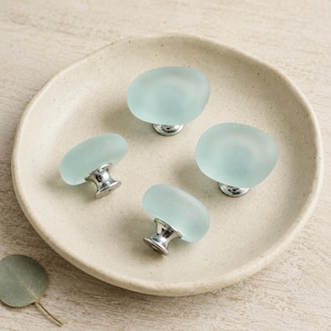 Peut inclure: Quatre boutons de placard dotés de sommets en verre dépoli vert mousse, lisses et arrondis, fixés sur des bases en métal argenté poli. Les boutons sont disposés en groupe, mettant en valeur leur finition translucide mate et leurs composants métalliques.