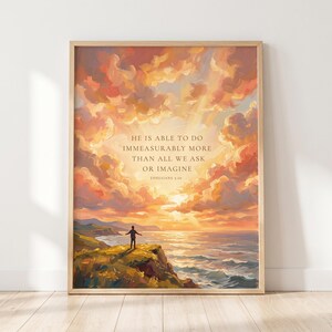Peut inclure: Une impression d'art encadrée représentant un paysage peint avec une personne debout sur une falaise surplombant l'océan au coucher du soleil. Le ciel est rempli de nuages orange et roses. Le texte indique : HE IS ABLE TO DO IMMEASURABLY MORE THAN ALL WE ASK OR IMAGINE EPHESIANS 3:20.