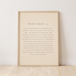Peut inclure: Une affiche murale encadrée présentant le texte des Proverbes 31 dans une police à empattement sur un fond beige clair. L'impression est insérée dans un cadre en bois clair, affichant le passage biblique complet en lettres noires sur le papier neutre.