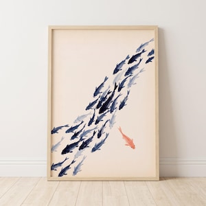 Könnte beinhalten: Ein gerahmter Wandkunstdruck mit einem Aquarellgemälde eines großen Schwarms dunkelblauer Fische, die diagonal über einen hellcremefarbenen Hintergrund schwimmen, wobei ein einzelner korallenfarbener Fisch unten rechts in die entgegengesetzte Richtung schwimmt.