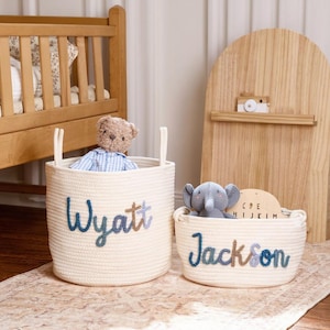 Peut inclure: Deux paniers de rangement en corde tressée blanc cassé avec anses. Le plus grand panier porte le nom Wyatt en lettres bleues et brunes, contenant un ours en peluche. Le plus petit porte le nom Jackson en lettres bleues et brunes, avec un éléphant.