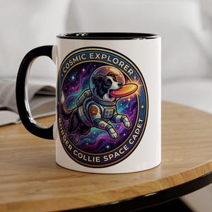 May include: A white ceramic mug with a black handle and interior rim. The mug features a circular graphic of a Border Collie wearing a space suit and helmet, floating in a colourful nebula while catching a flying disc, with the text COSMIC EXPLORER BORDER COLLIE SPACE CADET.
