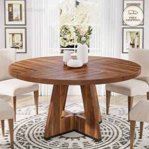 Può includere: Un tavolo da pranzo rotondo in legno con una ricca venatura marrone, sostenuto da una base geometrica centrale. Il tavolo presenta un piano circolare liscio ed è circondato da quattro sedie imbottite in tessuto beige chiaro.