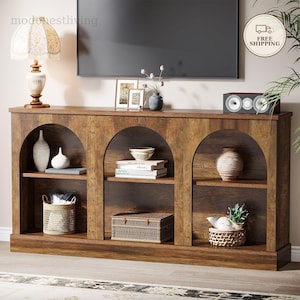 Puede incluir: Una mesa consola de madera marrón oscuro con tres secciones de estantería abiertas en forma de arco. El mueble tiene un acabado liso y ofrece varios niveles para almacenamiento y exhibición, conteniendo diversos objetos decorativos.