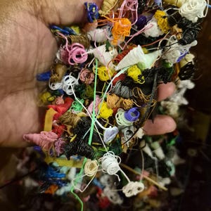 May include: A collection of tangled 3D printing filament waste in various colors including white, black, yellow, orange, pink, blue, and green. The plastic strands are coiled, knotted, and intertwined in a dense, irregular mass of discarded material.