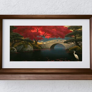 May include: A framed landscape print featuring a stone arched bridge over a dark pond, a vibrant red maple tree, and a white heron standing in the water. The artwork is enclosed in a dark brown wooden frame with a white mat, displayed on a shelf.