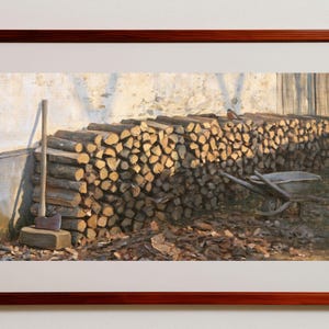 Puede incluir: Un cuadro de paisaje enmarcado que representa una gran pila de leña cortada contra una pared clara. Un hacha con un mango largo de madera descansa contra la pila de leña y una carretilla de metal se encuentra cerca sobre un suelo cubierto de hojas.