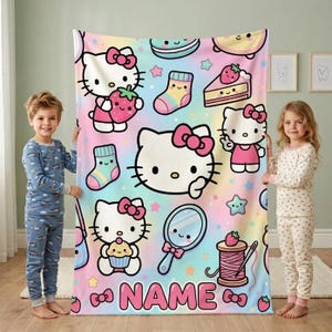 May include: A soft fleece blanket featuring a pastel rainbow gradient background with Hello Kitty characters, strawberries, cupcakes, socks, mirrors, and sewing spools. The bottom of the blanket includes the text NAME in pink letters.