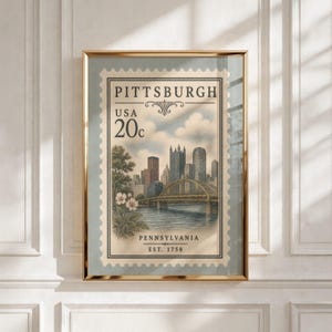 May include: A framed wall art print featuring a vintage-style postage stamp design of the Pittsburgh skyline. The image displays a bridge over a river, city skyscrapers, and flowers, with text reading PITTSBURGH, USA, 20c, PENNSYLVANIA, EST. 1758.