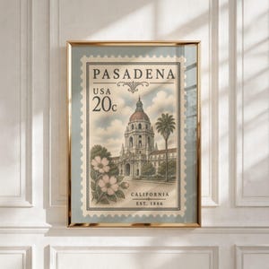 Op de afbeelding: Een ingelijste kunstdruk met een postzegelontwerp in vintage-stijl van Pasadena, Californië. De postzegel toont de tekst PASADENA, USA 20c, CALIFORNIA en EST. 1886, met een illustratie van een gebouw met koepel, een palmboom en bloemen.