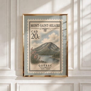 May include: A framed wall art print featuring a vintage-style postage stamp design of Mont-Saint-Hilaire, Quebec. The illustration depicts a mountain, a lake, and flowers, with text reading MONT-SAINT-HILAIRE, CAD 20c, QUÉBEC, and EST. 1642.