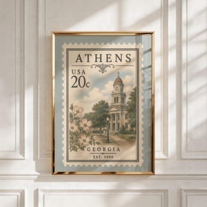 May include: A framed print of a postage stamp featuring the text ATHENS, USA, 20c, GEORGIA, and EST. 1806. The stamp depicts a multi-story building with a clock tower, surrounded by trees and a cluster of light pink dogwood flowers in the foreground.