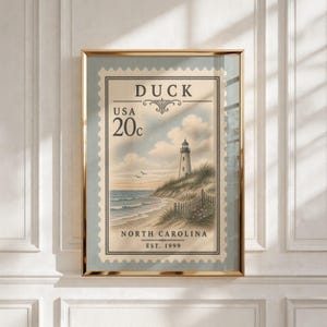 Puede incluir: Una impresión artística enmarcada con un diseño de sello postal de estilo vintage. La imagen muestra un faro en una duna cubierta de hierba con vistas al océano, con el texto DUCK, USA, 20c, NORTH CAROLINA y EST. 1999 en tinta negra.