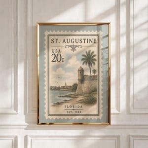 Könnte beinhalten: Ein gerahmter Kunstdruck mit einem Briefmarken-Design im Vintage-Stil von St. Augustine, Florida. Die Illustration zeigt einen steinernen Festungsturm, eine Palme und eine Küstenlandschaft mit dem Text ST. AUGUSTINE, USA 20c und EST. 1565.