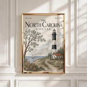 Op de afbeelding: Een poster in vintage-stijl getiteld The North Carolina Social gedateerd 22 juni 1934, met een zwart-witte vuurtoren, een klein huis met een rood dak, een zeilboot op het water, een grote boom en bloemen, in een gouden metalen lijst.