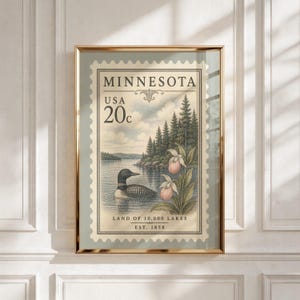 Könnte beinhalten: Ein gerahmter Kunstdruck im Design einer Vintage-Briefmarke mit einem Eistaucher auf einem See, einem Kiefernwald und rosa Frauenschuh-Blüten. Der Text lautet MINNESOTA, USA, 20c, LAND OF 10,000 LAKES und EST. 1858 in einer klassischen Schriftart.
