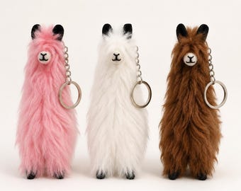 May include: Three fluffy llama keychains in pink, white, and brown. Each keychain features long, soft faux fur, black ears, a stitched face with a small nose and mouth, and a silver-toned metal chain with a circular ring for attachment.