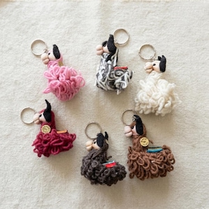 May include: A collection of six llama-shaped keychains crafted from textured yarn in pink, grey, white, dark red, dark brown, and light brown. Each keychain features a metal ring and a small circular tag labeled Made in Peru attached to the side.