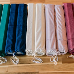 May include: A collection of ten long, cylindrical fabric covers arranged in pairs, featuring colors of teal, navy blue, cream, light pink, and deep red. Each cover has a soft, velvet-like texture and includes a white drawstring closure.