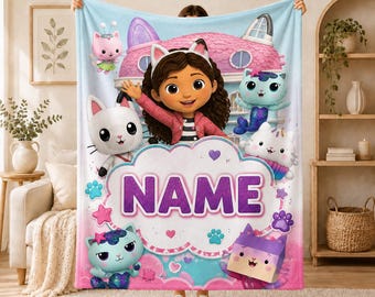 May include: A soft fleece blanket featuring a colourful Gabby's Dollhouse graphic with Gabby in the centre, surrounded by animated cat characters, paw prints, and stars. A large white cloud-shaped graphic in the middle contains the text NAME.