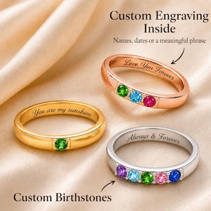 Puede incluir: Tres anillos de metal con piedras de nacimiento y grabados personalizados. Un anillo dorado con una piedra verde y 'You are my sunshine', uno de oro rosa con tres piedras y 'Love You Forever', y uno plateado con cinco piedras y 'Always & Forever'.