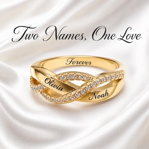 Puede incluir: Un anillo dorado de estilo infinito con dos bandas entrelazadas, una engastada con pequeñas piedras claras y la otra grabada con los nombres Olivia y Noah. La banda interior tiene grabado el nombre Forever. El texto superior dice Two Names, One Love.