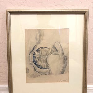 May include: A framed drawing featuring a blue ink sketch of a round plate and a handled pitcher on a light beige background. The artwork is enclosed in a metallic silver frame with a wide off-white matting. The artist's signature is visible.