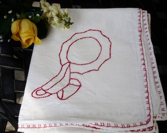 May include: White tea towel with a red embroidered design of a hand holding a mirror. The towel has a red stitched border.