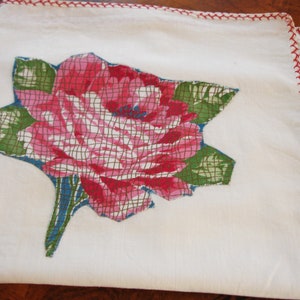 Pode incluir: Toalha de chá branca com uma borda vermelha bordada e um desenho floral rosa e verde.