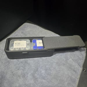 May include: A rectangular black storage container with a sliding lid, containing two clear plastic cases. The left case holds small vials with a label reading RT20 10vial/box for research use only, while the right case contains blue caps.