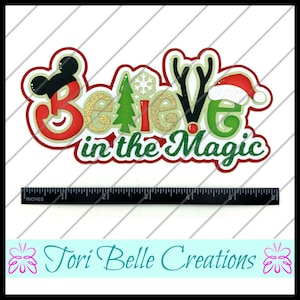 Puede incluir: Un dise&ntilde;o navide&ntilde;o en capas con las palabras "Believe in the Magic". La palabra "Believe" est&aacute; decorada con una cabeza de Mickey Mouse, un &aacute;rbol de Navidad y cuernos de reno. La palabra "Magic" tiene un gorro de Pap&aacute; Noel. El dise&ntilde;o mide aproximadamente 15 cm de largo.