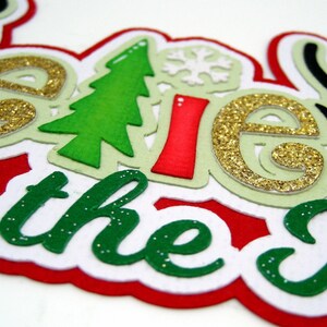 Puede incluir: Decoraci&oacute;n navide&ntilde;a festiva con la frase "Believe in the Magic of Christmas". Las letras son de purpurina dorada, verde, roja y blanca, con detalles de &aacute;rbol de Navidad y copo de nieve.