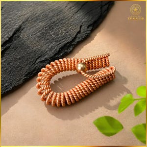 May include: A copper-colored bracelet formed from a continuous, tightly coiled wire structure. The bracelet features a smooth, spherical bead at the point where the two ends of the coiled wire meet, creating a secure, circular loop design.