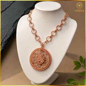 May include: A copper-colored necklace featuring a large, circular pendant with an intricate, woven wire pattern and a central spiral design. The chain is composed of interconnected circular links, each joined by small, spherical metal beads.