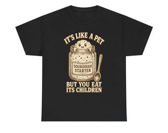 May include: A black t-shirt featuring a graphic of a glass jar containing sourdough starter with a smiling character emerging from the top. The text reads IT'S LIKE A PET BUT YOU EAT ITS CHILDREN and SOURDOUGH STARTER, accompanied by a wooden spoon.