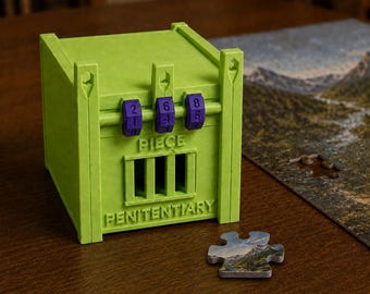May include: A lime green plastic box shaped like a jail cell with three purple rotating number dials on the front. The word PIECE is embossed above a barred window, and the word PENITENTIARY is embossed below it. A single puzzle piece sits nearby.