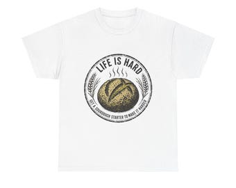 May include: A white short-sleeve t-shirt featuring a circular graphic on the chest. The design shows a golden-brown sourdough loaf with steam lines, surrounded by wheat stalks and the text "LIFE IS HARD" and "GET A SOURDOUGH STARTER TO MAKE IT HARDER."