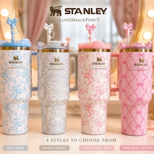 May include: Four Stanley LoveShackFancy tumblers with handles and straws topped with bow charms. The designs include blue bows, white floral patterns, pink floral bows, and a pink bow lattice. Each stainless steel cup features the brand logo.