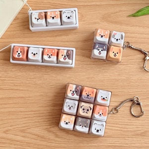 May include: A collection of mechanical keyboard keycap accessories featuring various dog faces. The set includes a three-key row, a four-key square, and a nine-key square, all with white bases and colorful cartoon dog illustrations on each keycap.