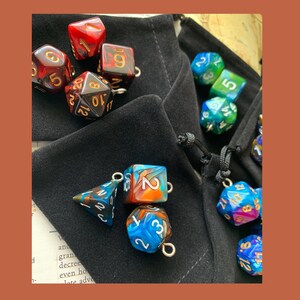 May include: A collection of colorful dice with gold accents, some are in a black velvet bag, others are scattered on a table. The dice are multi-sided and have different numbers on each side.