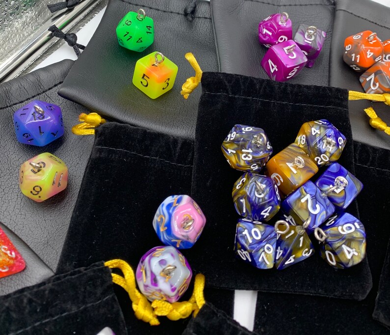 May include: A collection of colorful dice in various shapes and sizes, including a set of blue and gold dice with white numbers, a set of yellow and blue dice with white numbers, and a set of green and white dice with black numbers. The dice are arranged in a variety of patterns and are displayed on a black velvet surface.