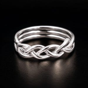 May include: A polished silver-toned ring featuring a continuous braided or woven design that encircles the entire band. The metal surface is smooth and reflective, showcasing a series of interlocking loops that create a textured, knotted appearance.