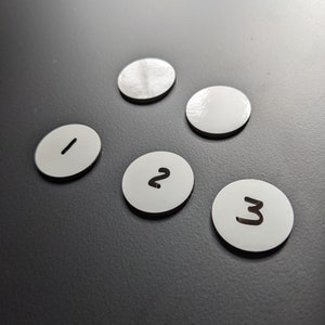 May include: Five white round game pieces with black numbers 1, 2, and 3. Two pieces are blank.