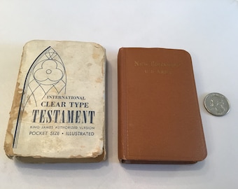 Puede incluir: Dos pequeños libros encuadernados en cuero marrón. El libro de la izquierda tiene una cubierta blanca con una ilustración azul de una ventana de vitrales y el texto "International Clear Type Testament King James Authorized Version Pocket Size Illustrated". El libro de la derecha tiene el texto "New Testament" en la cubierta.
