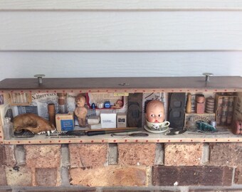 May include: A wooden box filled with various objects, including a doll's head, a skull, dice, and a small bottle. The box is decorated with red and white polka dots and has a brown lid.