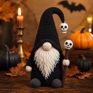 May include: A crocheted gnome featuring a tall black pointed hat with a dangling white skull charm, a long cream-colored yarn beard, and a beige nose. The gnome holds a brown staff topped with a white skull and wears dark gray rounded feet.