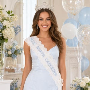 Puede incluir: Un vestido sin mangas de color azul claro con una banda de encaje blanco que presenta el texto MISS NORTH CAROLINA bordado en azul. La prenda se combina con una corona de metal plateado adornada con cristales transparentes y filigrana.