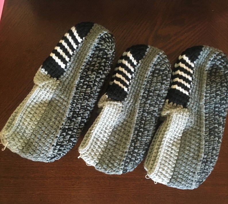 May include: Three pairs of gray and black crocheted slippers with white stripes.