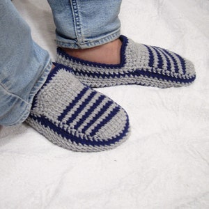 May include: A pair of gray and blue striped knitted slippers with a blue trim. The slippers are worn by a person wearing blue jeans.