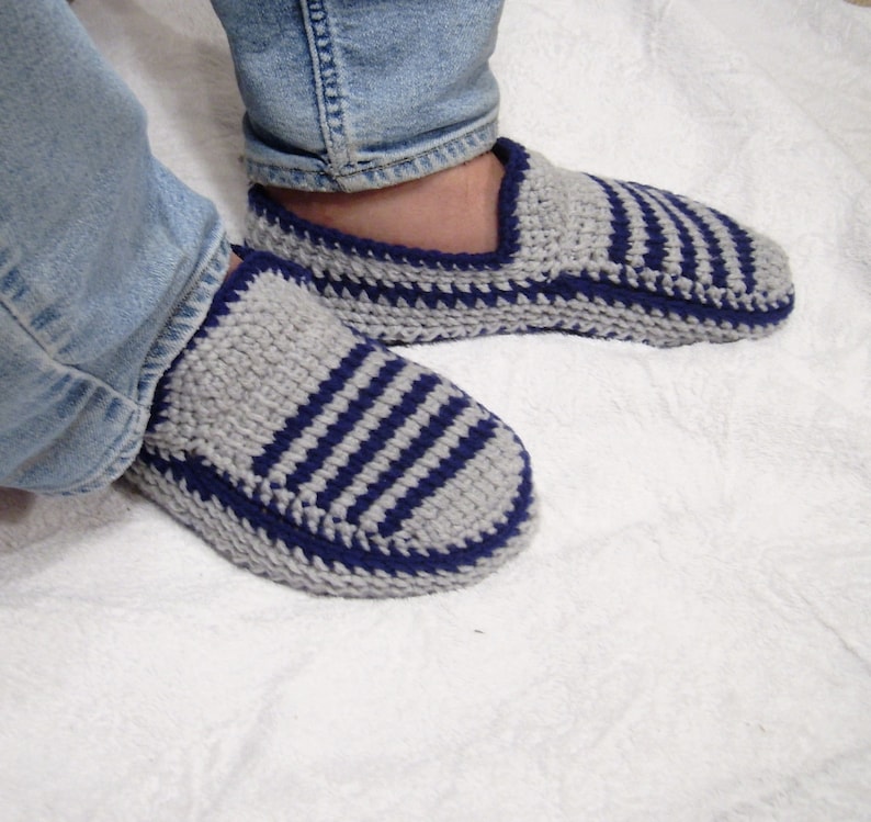 May include: A pair of gray and blue striped knitted slippers with a blue trim. The slippers are worn by a person wearing blue jeans.